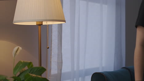 young-woman-is-switching-on-floor-lamp-in-living-room-at-evening-detail-shot-interior-and-furniture-of-room-of-cozy-apartment